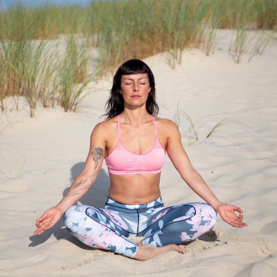 femme assise dans le sable en tenue de yoga qui médite au soleil