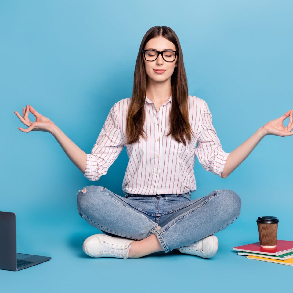 Portrait of beautiful trendy calm girl sitting doing homework meditating isolated over bright blue color background.