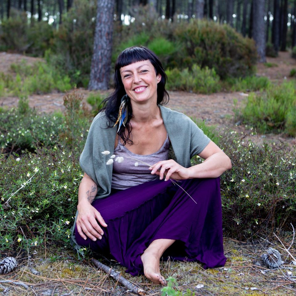 femme souriante assise dans la forêt avec des herbes à la main